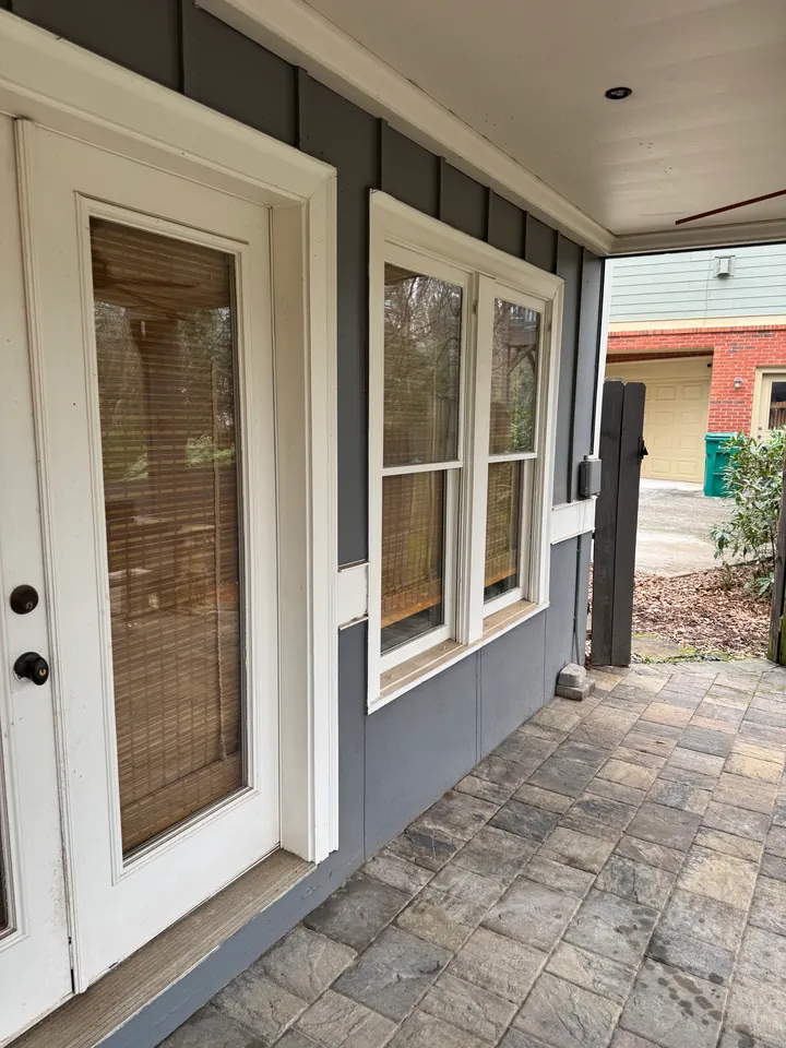 Covered porch with gray siding, white doors and window trim, and a paver floor.
