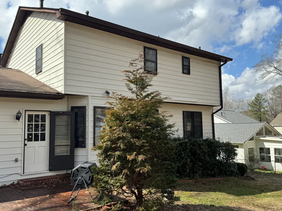 Cream two-story house exterior, dark trim, lawn and patio beneath a partly cloudy sky.