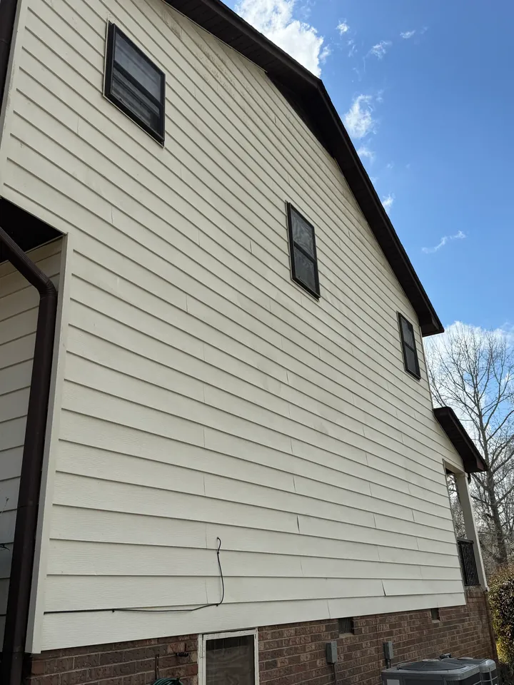Cream lap siding on a tall gable wall with windows and a brick foundation.